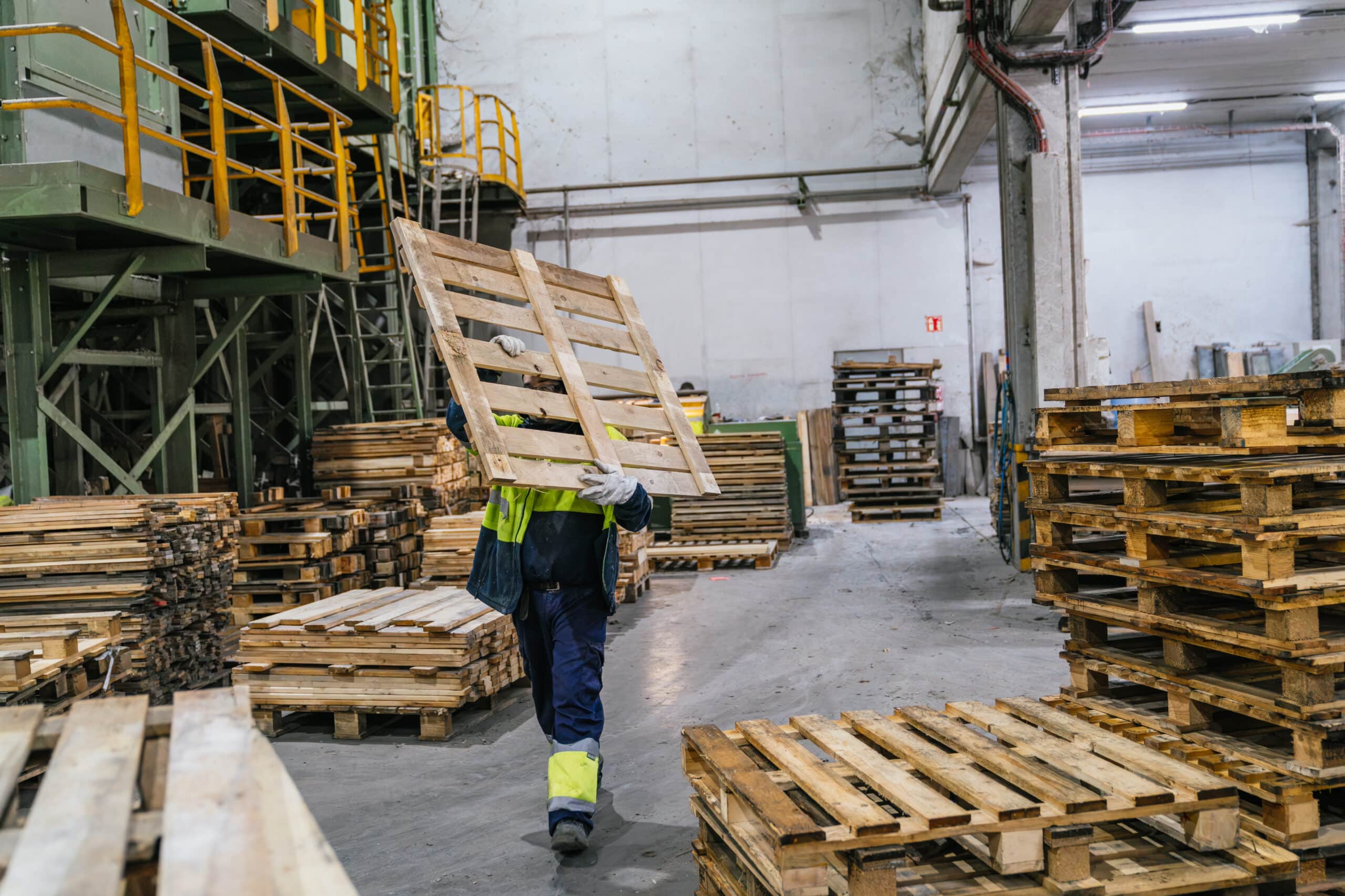 Factory worker carrying wooden pallet in recycling plant