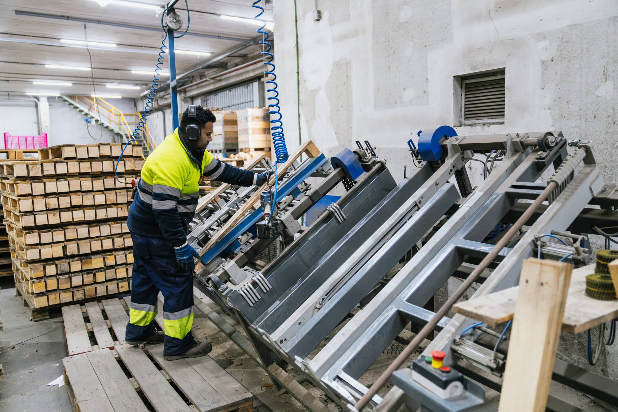 Factory worker assembling wooden pallets with industrial machinery