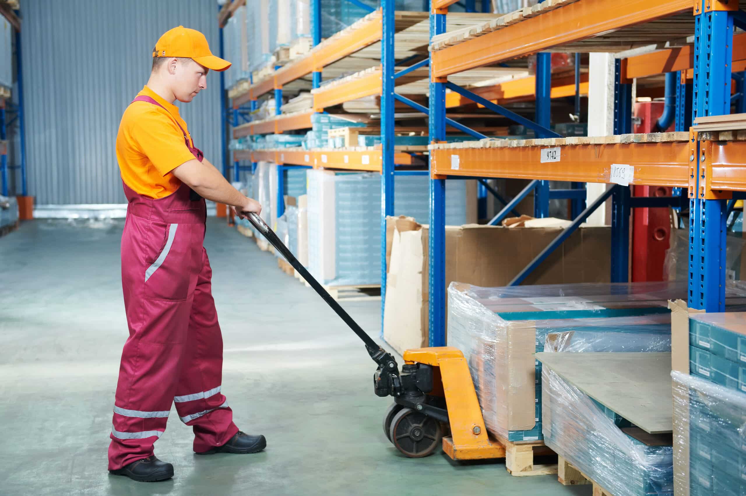 Worker with fork pallet truck stacker in warehouse loading furni