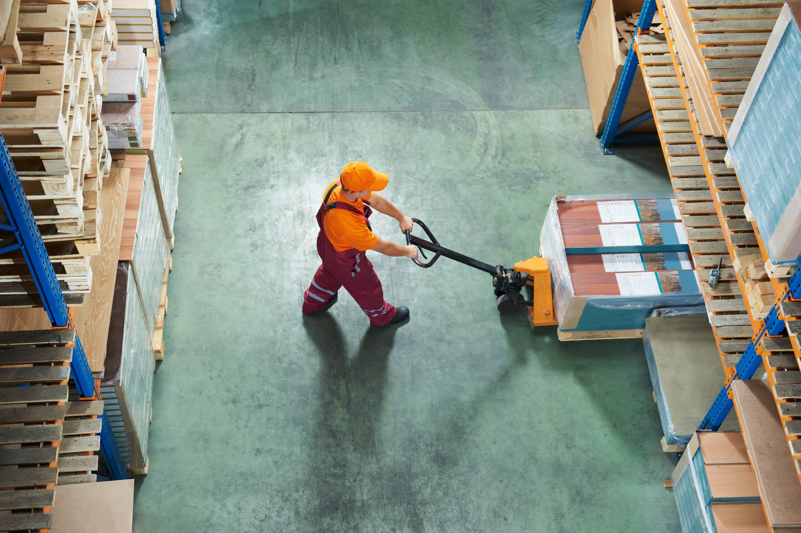 Worker with fork pallet truck stacker in warehouse loading furni